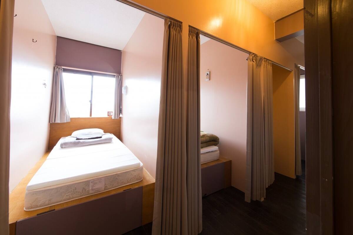 A small, compact hotel room with a single bed, a bedside table, and a window.