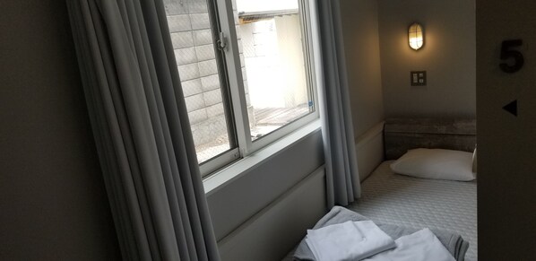 A hotel room with a bed, a window with curtains, a wall-mounted light, and a number indicating the room's location. - Little Barrel Guest House - Hostel (Otaru)