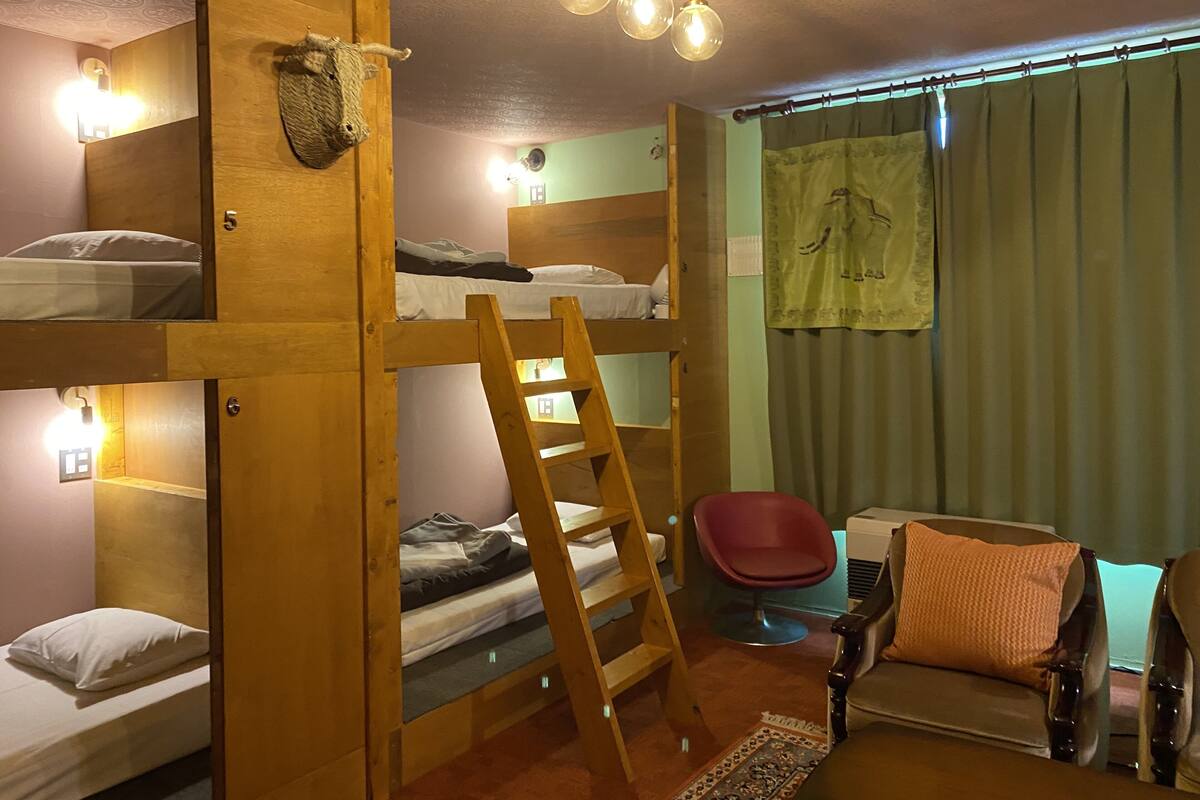 A room with bunk beds, a ladder, a red chair, a sofa, and a wall-mounted light fixture.
