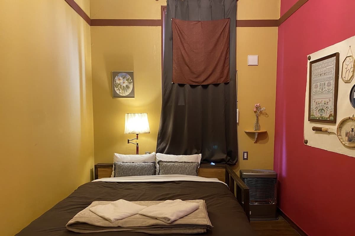 A hotel room with a bed, a nightstand, a lamp, a window with a curtain, and a wall with framed pictures.