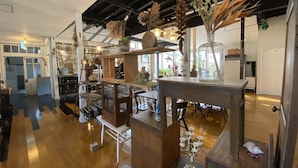 Un interior espacioso con techos altos y vigas a la vista, que presenta mobiliario de madera, vitrinas de vidrio y diversos objetos decorativos.