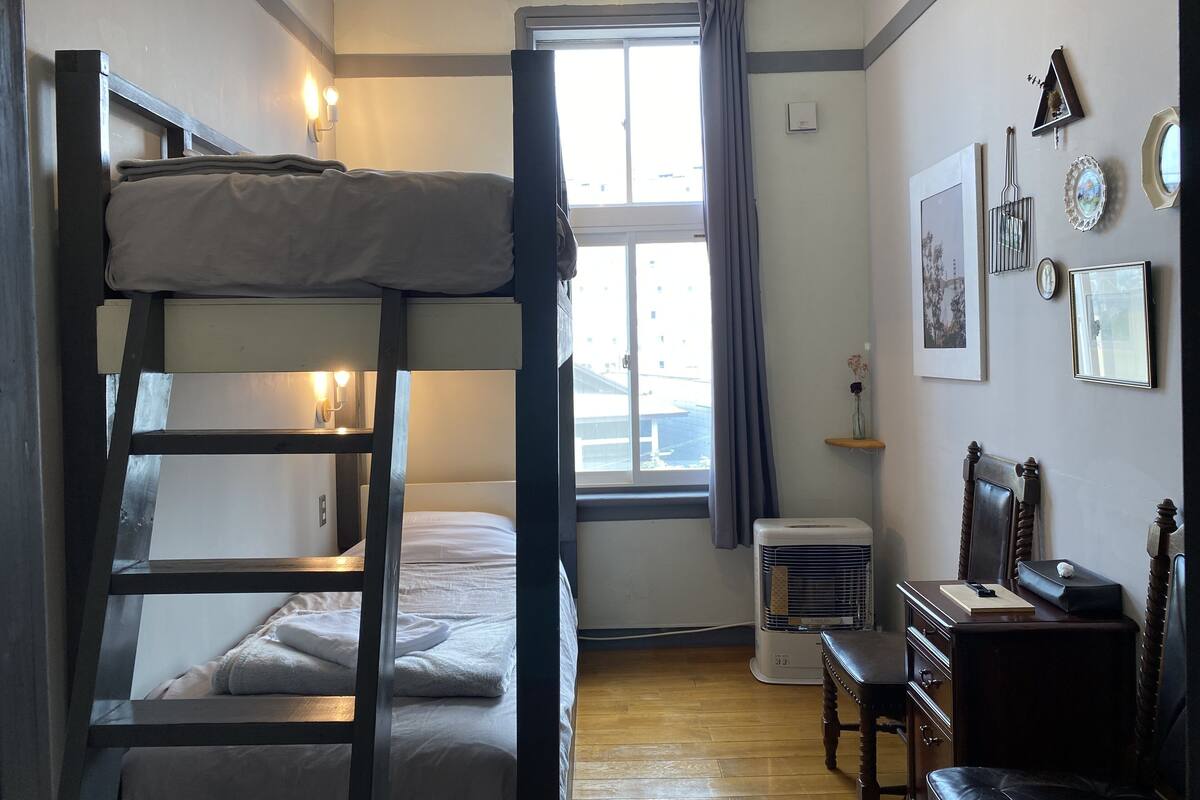 A bunk bed room with a desk, chair, and a window with curtains.