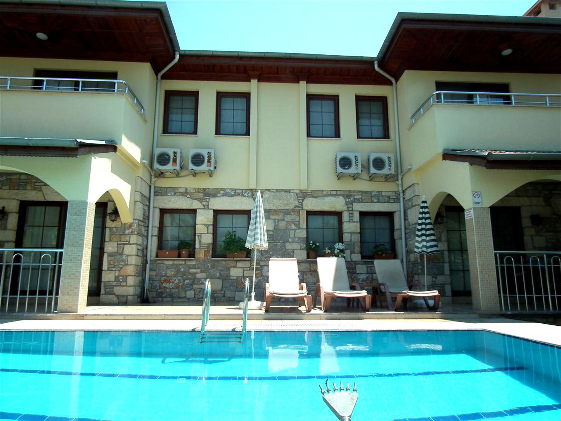 A hotel with a swimming pool, stone facade, and multiple air conditioning units.