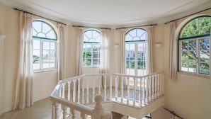 A spacious balcony with a white balustrade, large arched windows with curtains, and a view of greenery outside. - Spacious 4 bedroom villa in quiet location with sea views  (Almancil)