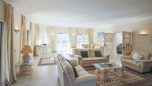 A spacious living room with a sofa, armchairs, and a coffee table. There is a kitchen area in the background and a door leading to another room. - Spacious 4 bedroom villa in quiet location with sea views  (Almancil)