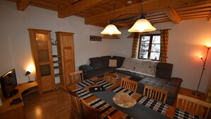 A cozy living room with a wooden dining table, chairs, a sofa, and a television. - Holiday home in a quiet location in the beautiful Carinthian Alps (Eissentratten)