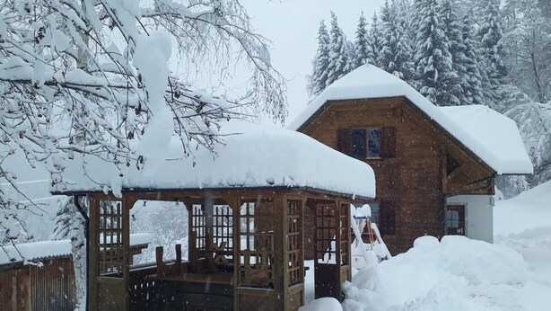 A wooden cabin with a snow-covered roof and a wooden gazebo in front. - Holiday home in a quiet location in the beautiful Carinthian Alps (Eissentratten)