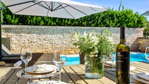 An outdoor dining area with a table set for two, a bottle of wine, and a vase of flowers.
