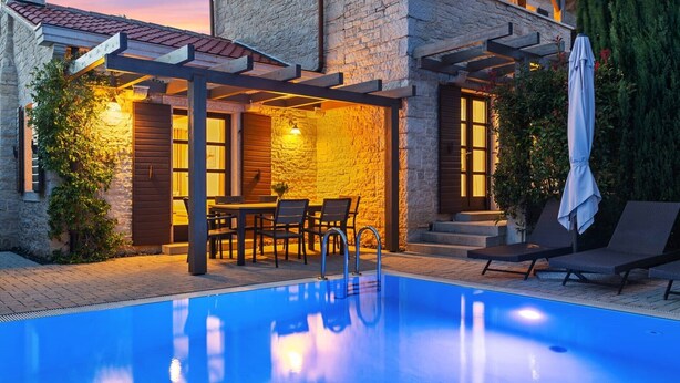 A swimming pool with a pergola and outdoor seating area, surrounded by stone walls and vegetation.