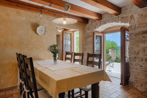 A dining area with a table set for two, wooden chairs, a vase with flowers, and a clock on the wall.
