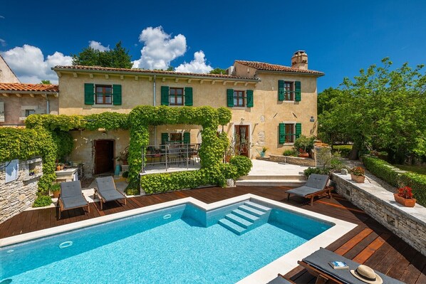 A villa with a swimming pool, outdoor seating, and a garden.