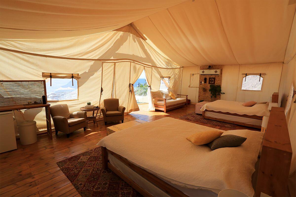 A tented accommodation with a large bed, a smaller bed, a desk, and a chair.