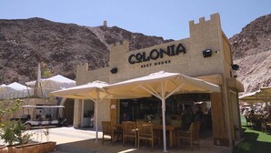 Un restaurante llamado 'Colonia Rest House' con terraza y telón de fondo de montañas.