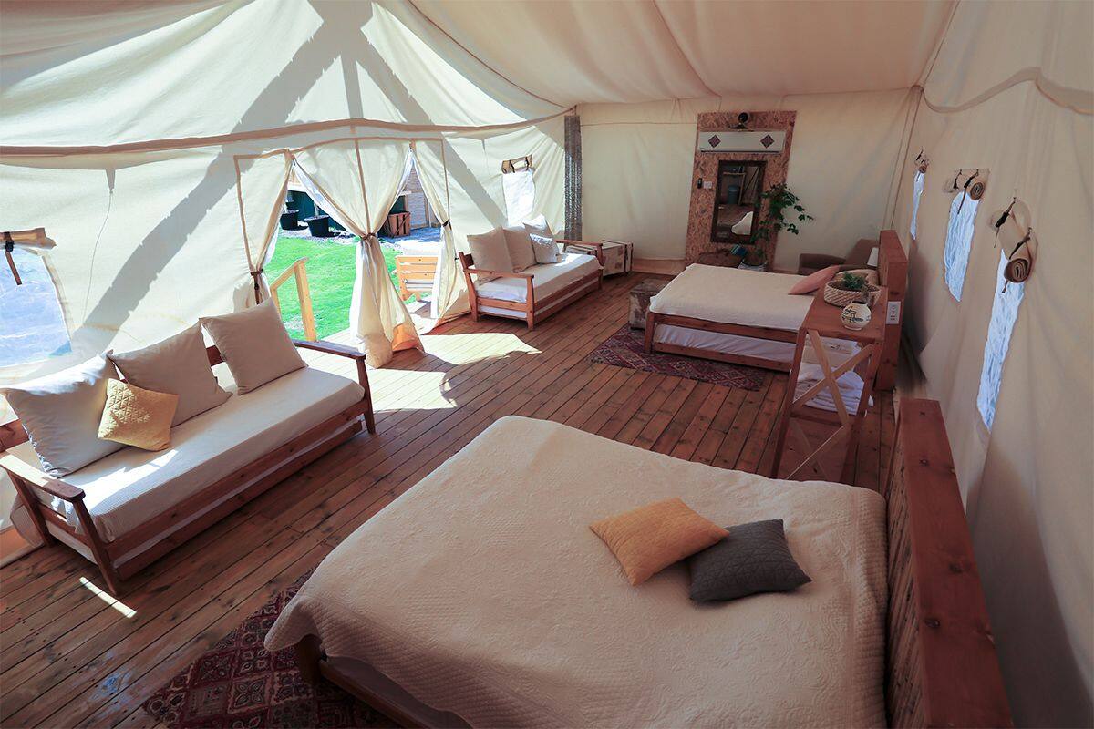 A tented accommodation with two beds, a sofa, and a small table.