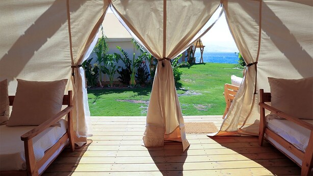 Una habitación con carpa, dos camas de madera y vista al océano.