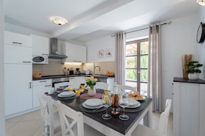 A modern kitchen with white cabinets, a dining table set for two, and a large window with curtains.