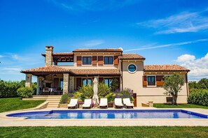 Una casa de dues plantes amb piscina, zona d'estar a l'exterior i jardí ben cuidat.