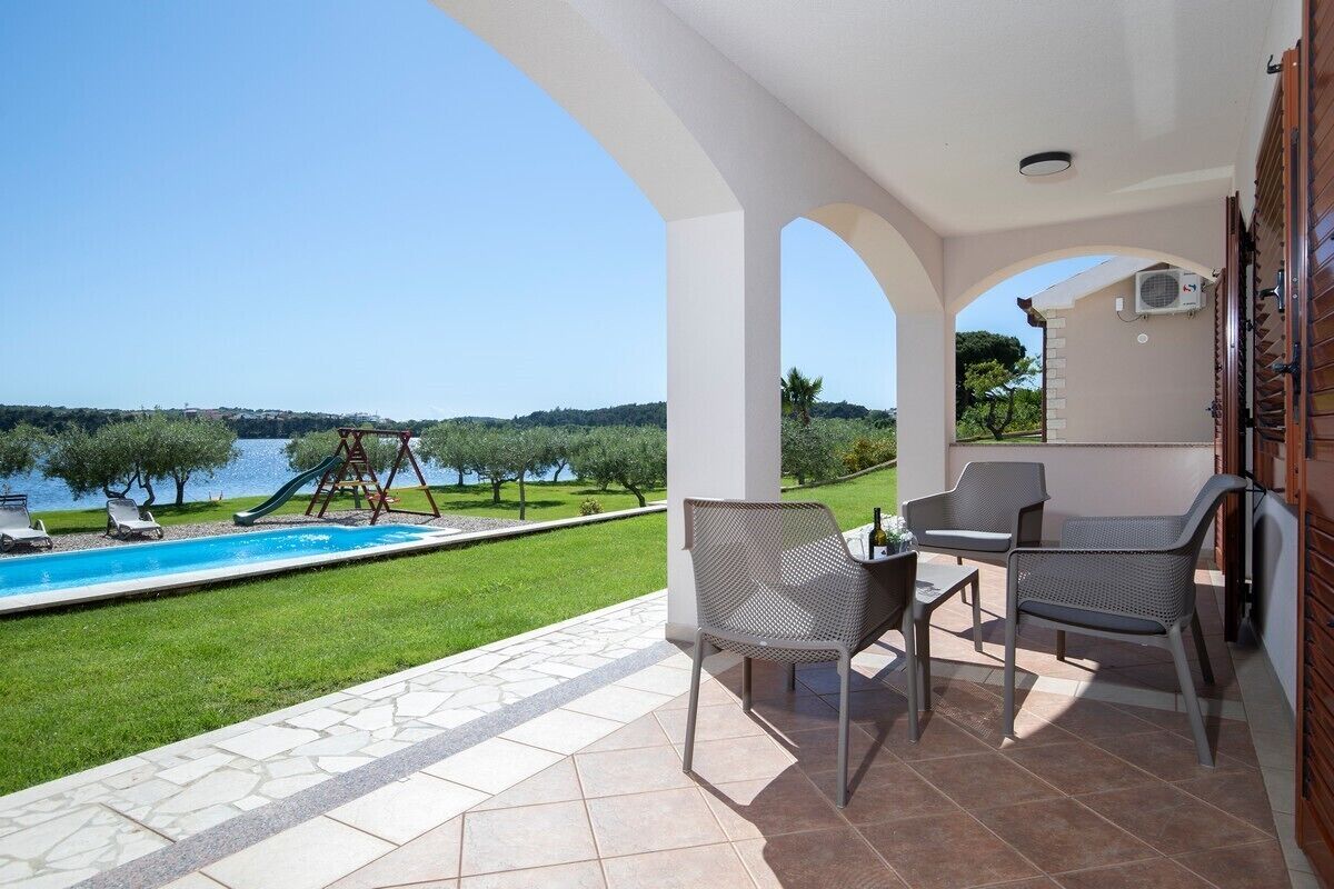 Une terrasse avec des sièges extérieurs, une piscine et une vue sur un lac et des arbres.