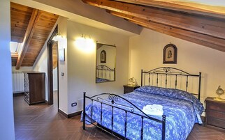 Una camera da letto con un letto, travi in legno a soffitto, un comodino e uno specchio fissato alla parete.