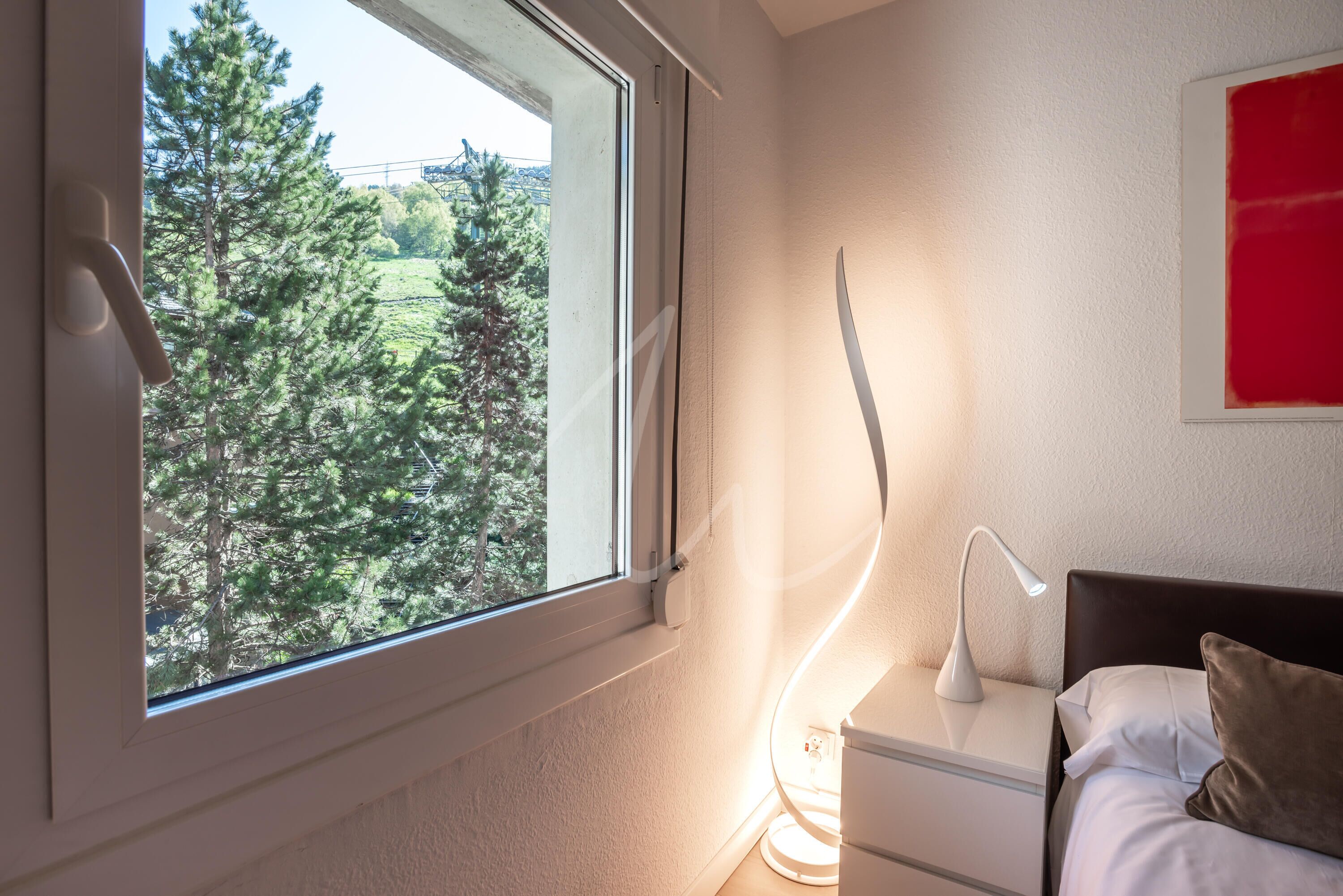 Un dormitorio con ventana, lámpara de noche y cama con almohadas.