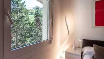 Un dormitorio con ventana, lámpara de noche y cama con almohadas.