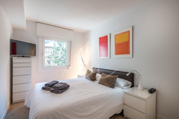 A neatly made bed with towels, a bedside lamp, and a TV on a stand.