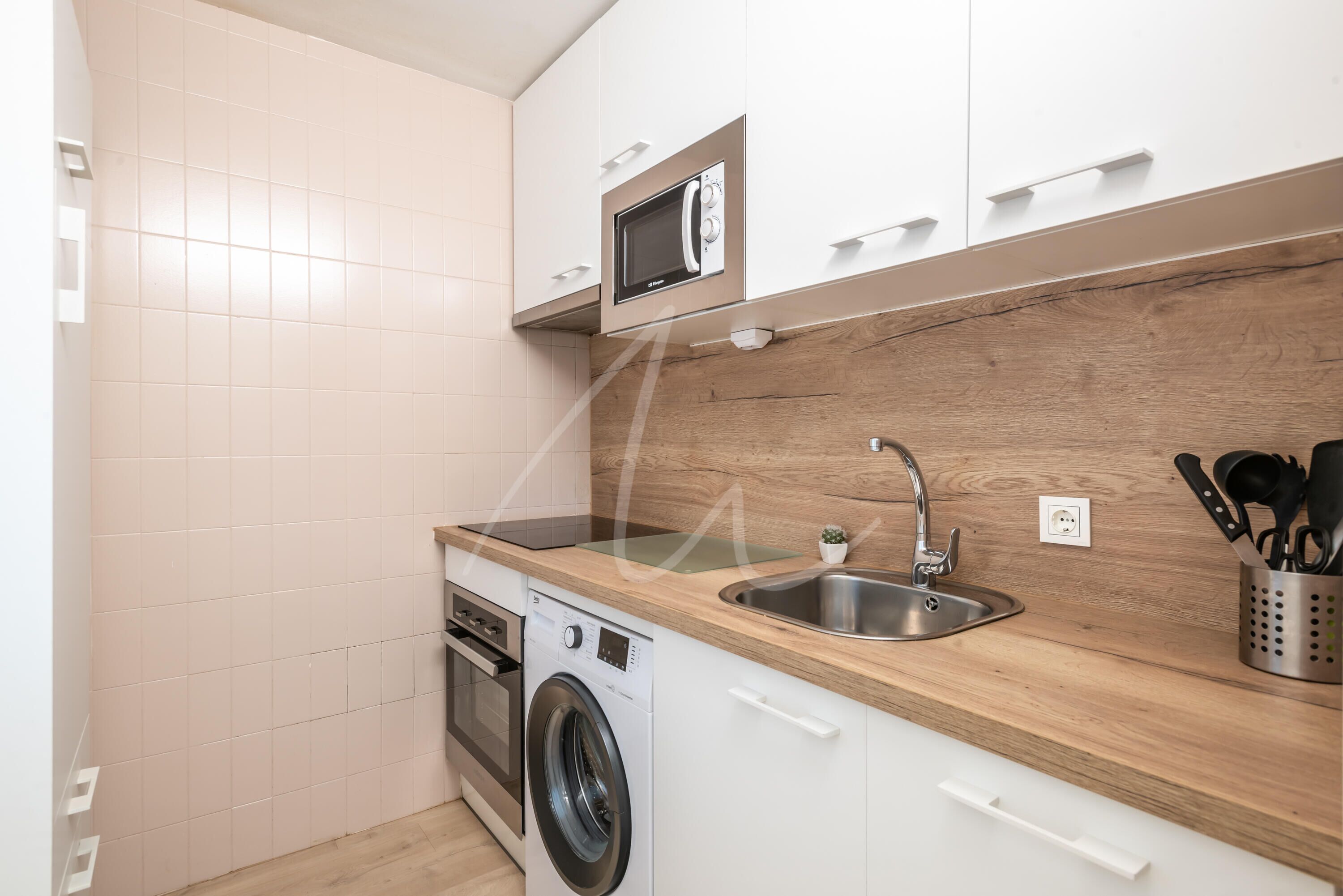 A compact kitchen with a washing machine, a microwave, and a sink.