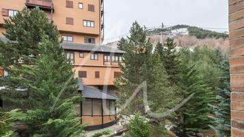 Un edificio de varios pisos con techo plano, rodeado de árboles de hoja perenne.
