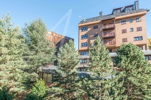 A multi-story building with balconies, surrounded by dense evergreen trees.
