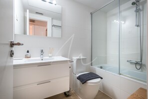 Moderni kylpyhuone, jossa on wc, pesuallas, peili ja lasiseinällä varustettu suihku.