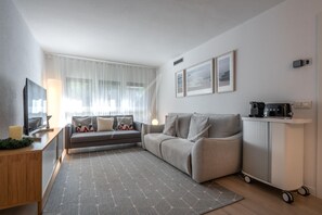 A modern living room with a sofa, a coffee table, a TV, and a cart with appliances.
