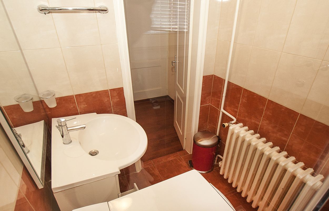 Une salle de bain avec un lavabo blanc, un miroir, un porte-serviettes, un radiateur et une poubelle.