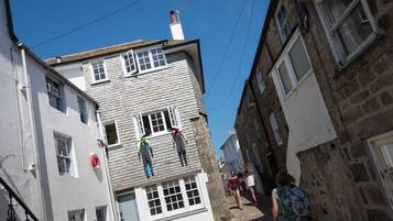 A narrow street with stone buildings, a person hanging laundry, and another person walking.