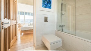 A modern bathroom with a glass shower enclosure, a white toilet, and a bed with a city view.