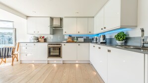 Een moderne keuken met witte kasten, een ingebouwde oven en een aanrecht met diverse apparaten.