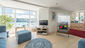Een moderne woonkamer met een groot raam dat uitkijkt op een haven, een flatscreen televisie, een comfortabele zithoek en een boekenkast.