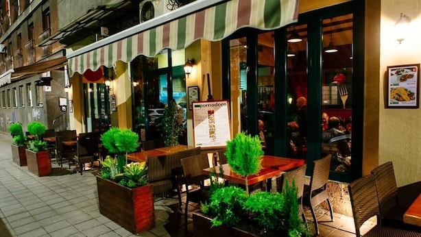 An outdoor café with tables and chairs, a striped awning, and a menu sign. - Apartment Art Galery (Belgrade)