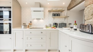 A modern kitchen with white cabinetry, a built-in oven, and a countertop with various appliances and fresh produce.