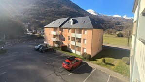 A multi-story building with balconies, a parking lot with cars, and a mountainous backdrop. - Charming Studio for 4 with Balcony, Parking & Ski Storage – Near Ski Resorts (Luz-Saint-Sauveur)