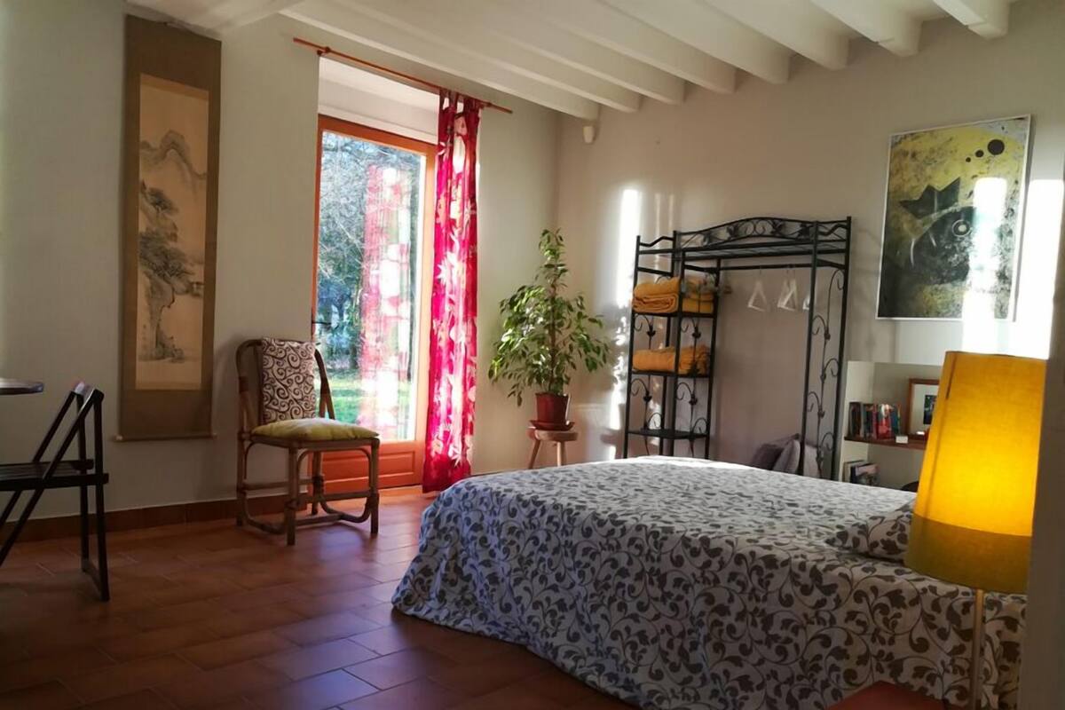 Quarto com cama, uma cadeira, planta, prateleira com toalhas e um quadro na parede.