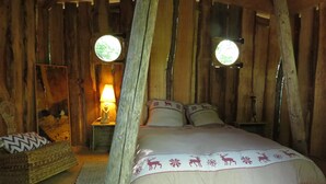 A rustic wooden room with a bed, a nightstand with a lamp, and a chair. There are two circular windows on the walls. - Tramois - Chambres d'hôtes (Donzy)