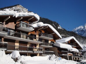 Een hotel met meerdere verdiepingen, balkons, besneeuwde daken en een bergachtige achtergrond.