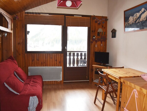 A cozy cabin interior with a wooden interior, a red sofa, a wooden dining table, and a television.