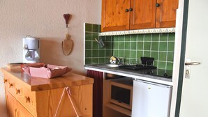 Een kleine keuken met houten kastjes, een kleine koelkast en een koffiezetapparaat op het aanrecht.