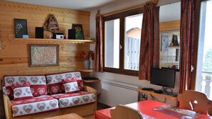 A cozy cabin-style room with a wooden sofa, a small wooden table, and a television on a wooden stand. - Cozy and bright apartment, 2 rooms, near slopes, 4 people (Pralognan-la-Vanoise)