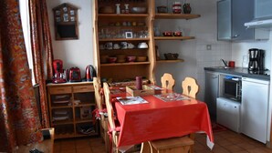 A compact kitchen with a dining area, featuring a wooden cabinet, a red tablecloth-covered table, and a microwave. - Cozy and bright apartment, 2 rooms, near slopes, 4 people (Pralognan-la-Vanoise)