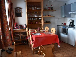 A compact kitchen with a dining area, featuring a wooden cabinet, a red tablecloth-covered table, and a microwave. - Cozy and bright apartment, 2 rooms, near slopes, 4 people (Pralognan-la-Vanoise)