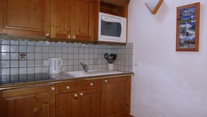 Eine Küche mit Holzausstattung, einer weißen Mikrowelle, einem Spülbecken und einer gefliesten Rückwand.