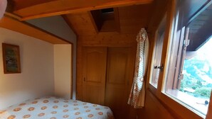 Ein Schlafzimmer mit Bett, Holzboden, einer Tür und einem Fenster mit Blick ins Freie.