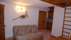 Ein gemütliches Zimmer mit einer Couch, einem Holztisch und einer Küche im Hintergrund.